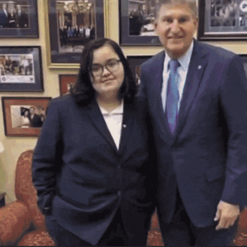 a man in a suit and tie poses with a woman in a suit and glasses