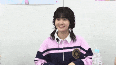 a girl wearing a pink and black striped sweater is smiling while holding her hands over her chest .