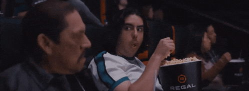 a man is eating popcorn in front of a regal bucket
