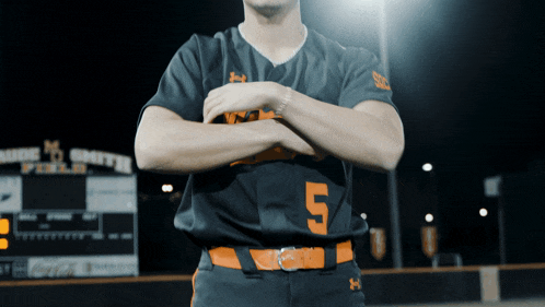 a baseball player stands with his arms crossed in front of a scoreboard that says smith field