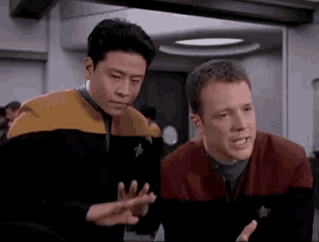 two men are standing next to each other in a room talking to each other .
