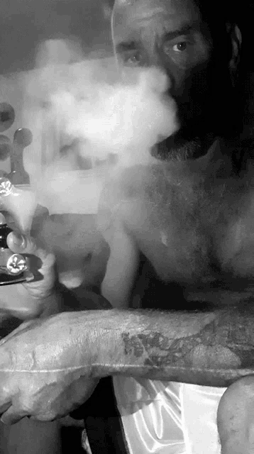 a shirtless man with a tattoo on his arm smoking a cigarette
