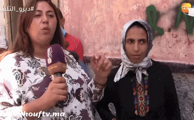 a woman is holding a purple microphone while talking to another woman in front of a sign that says houftv.ma