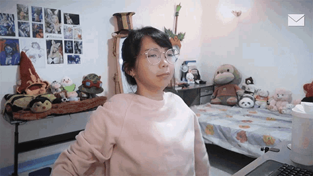 a woman wearing glasses stands in front of a bed with stuffed animals