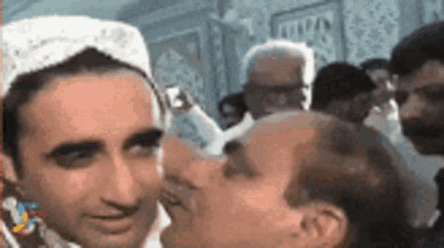a man in a white hat is kissing another man 's forehead .