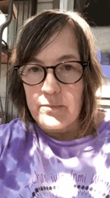 a woman wearing glasses and a purple shirt is taking a selfie .