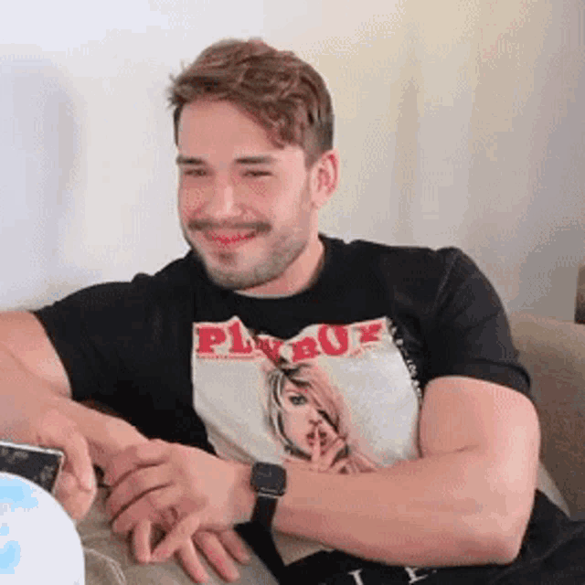 a man wearing a playboy shirt is sitting on a couch .