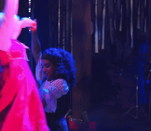 a woman in a pink dress is dancing with another woman in a white wig