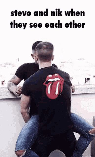 a man wearing a rolling stones shirt is sitting on another man 's lap