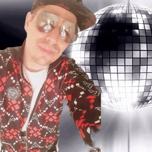 a man wearing sunglasses and a hat stands in front of a disco ball with the letter a on it