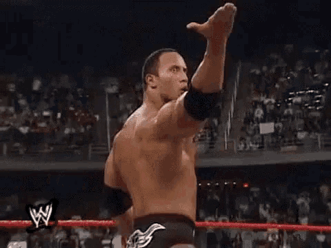 a shirtless wrestler is standing in a wrestling ring with his arm in the air .