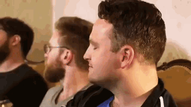 a group of men are sitting on a couch and one of them is looking at the camera .