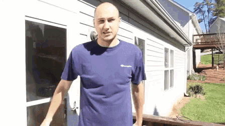 a bald man in a purple champion shirt is standing in front of a white house .