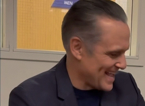 a man is smiling in front of a men 's restroom sign