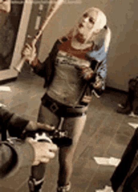 a woman in a harley quinn costume is holding a bat and a remote control .