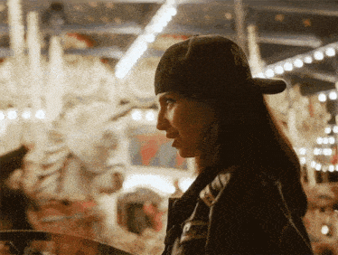 a woman wearing a black hat with the letter n on it stands in front of a merry go round