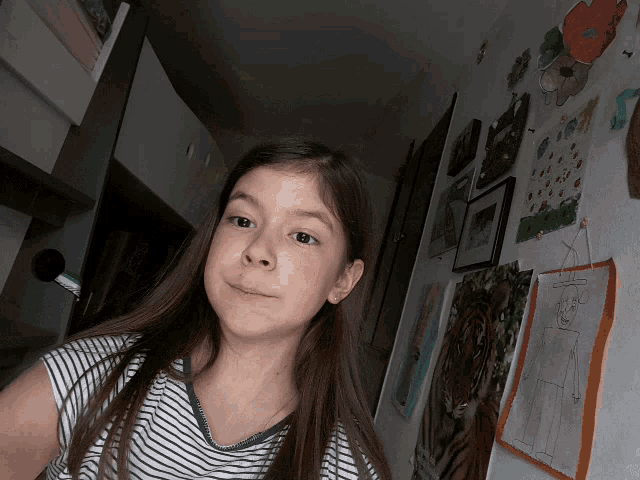 a girl in a striped shirt is standing in front of a wall with paintings on it