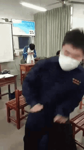 a man wearing a mask is standing in a classroom with other people