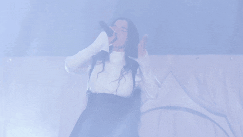 a woman with long hair singing into a microphone in a dark room