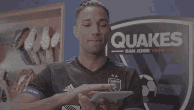 a man in an adidas shirt holds a box in front of a sign that says quakes
