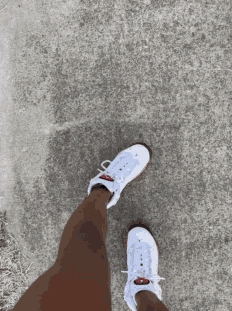 a person wearing a pair of white shoes with red laces walking on a sidewalk
