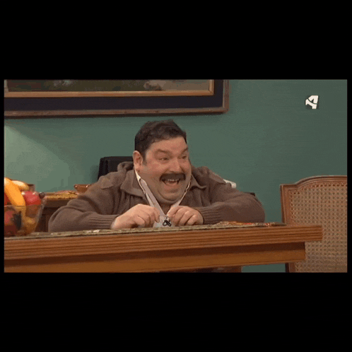 a man sits at a table with his head on the table and a sign that says tv on the wall behind him