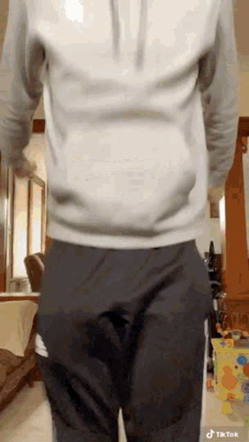 a man wearing a white hoodie and black pants is standing in a room with his hands in his pockets .