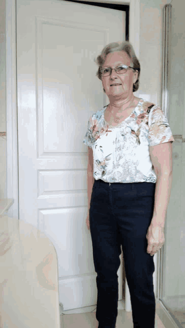 a woman wearing glasses and a floral shirt is standing in front of a white door
