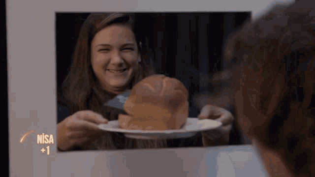 a woman holding a plate with a loaf of bread in front of a screen that says nisa + 1