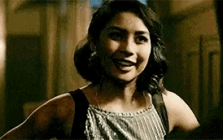 a woman in a striped tank top is smiling and looking at the camera in a dark room .