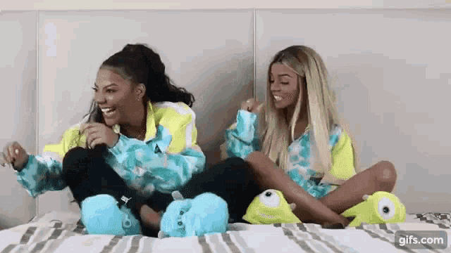 two women are sitting on a bed with their legs crossed and wearing slippers .