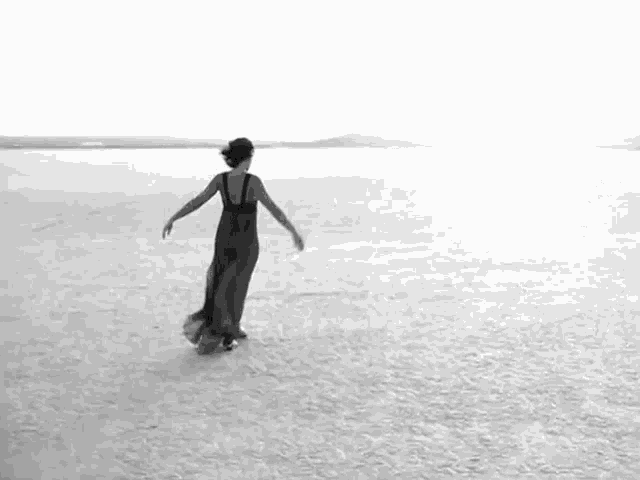a black and white photo of a woman in a long dress dancing in a desert .