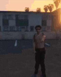 a man without a shirt is standing in a parking lot at sunset