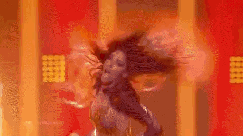 a woman is dancing in a room with fire coming out of her hair .