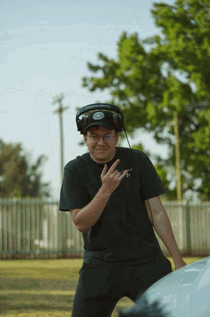 a man wearing headphones and a black shirt with the letter t on it is giving a peace sign