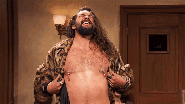 a man with long hair and a beard is laughing and holding his chest
