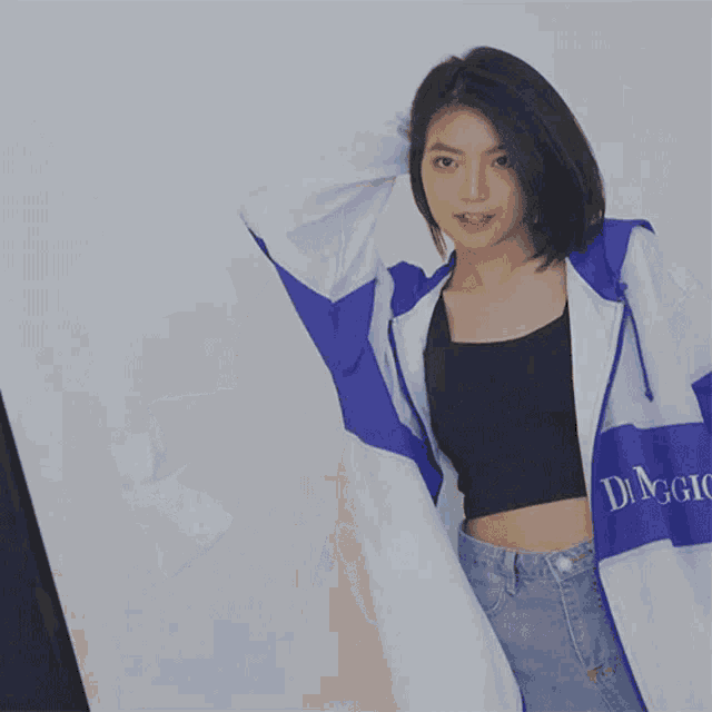 a blurry picture of a woman wearing a blue and white jacket and a black crop top .