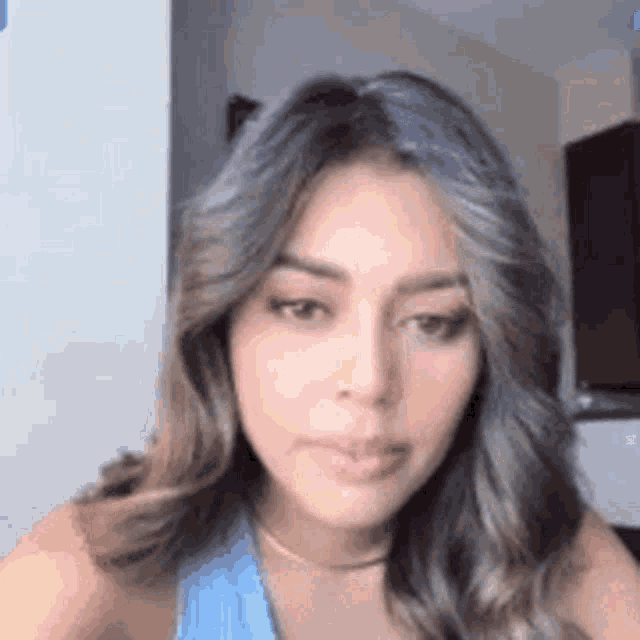 a woman with long hair is looking at the camera while wearing a blue tank top .