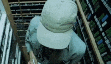 a man wearing a hat and a blue shirt is standing in a room filled with shelves .