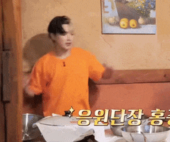 a man in an orange shirt is standing in front of a table with bowls and a picture on the wall above him .