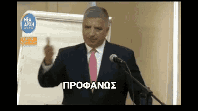 a man in a suit and tie stands in front of a microphone with the word profanos on the screen