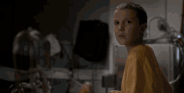 a young girl in a yellow shirt is sitting in a dark room looking at something .