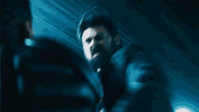 a man with a beard and mustache is standing in a dark room holding a gun .