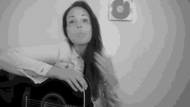 a black and white photo of a woman playing an acoustic guitar in front of a wall .