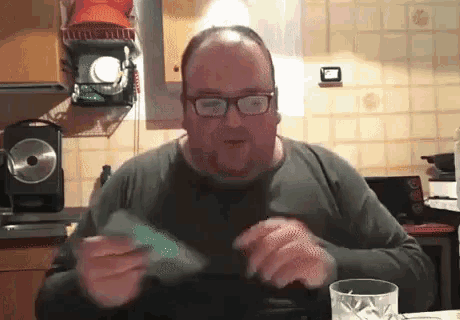 a man with glasses is sitting at a table in a kitchen