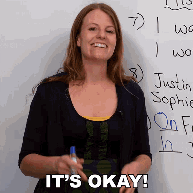 a woman standing in front of a white board with the words it 's okay written on it