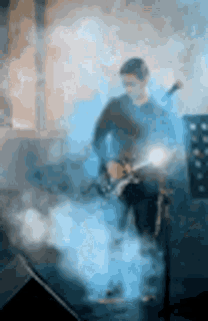 a man is playing a guitar on a stage with smoke coming out of it .