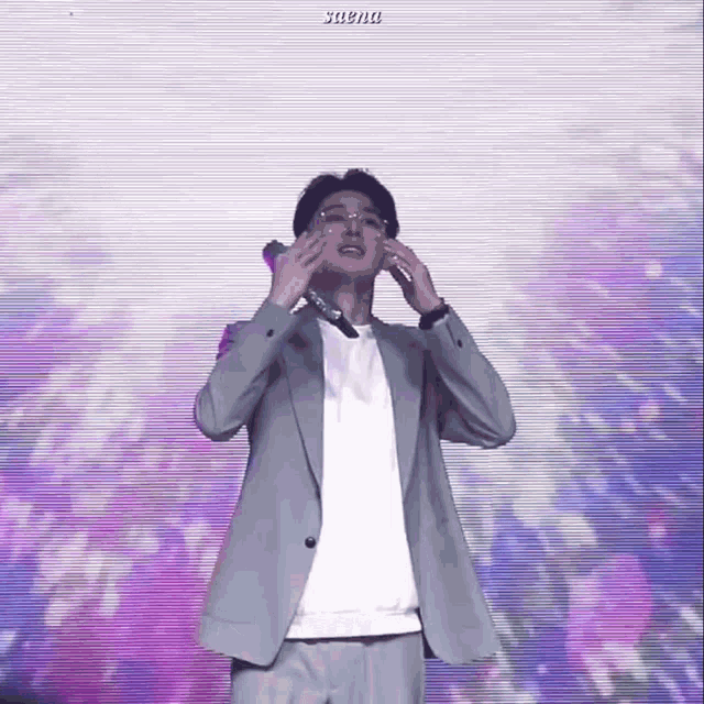 a man in a suit and glasses is holding a microphone in front of a screen that says saena