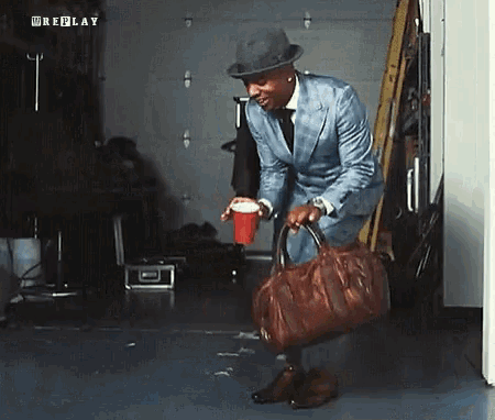 a man in a suit and hat is holding a red cup and a brown bag and the word replay is on the bottom right