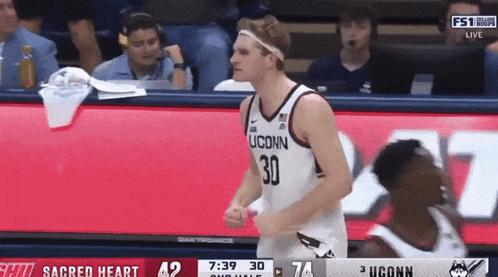 a man wearing a uconn jersey stands on a basketball court